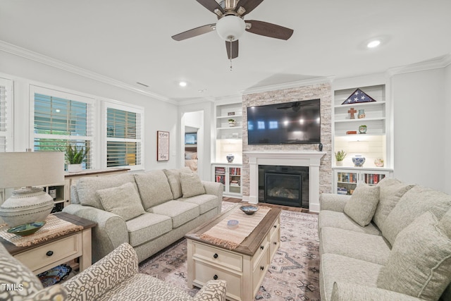 living room with ornamental molding, a stone fireplace, ceiling fan, and built in shelves