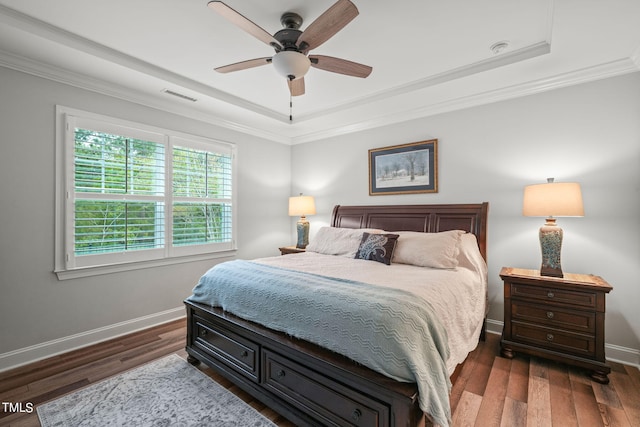 bedroom with crown molding, dark wood-type flooring, a raised ceiling, and ceiling fan