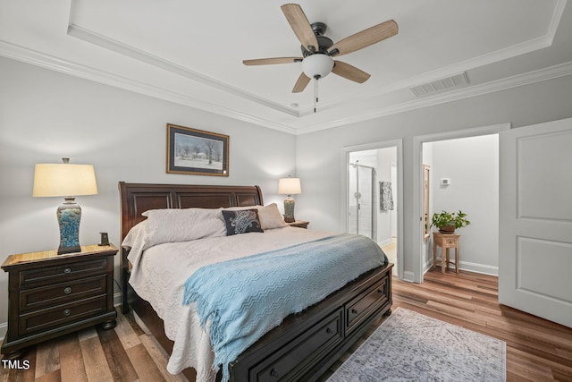 bedroom featuring ensuite bathroom, wood-type flooring, ceiling fan, a tray ceiling, and crown molding