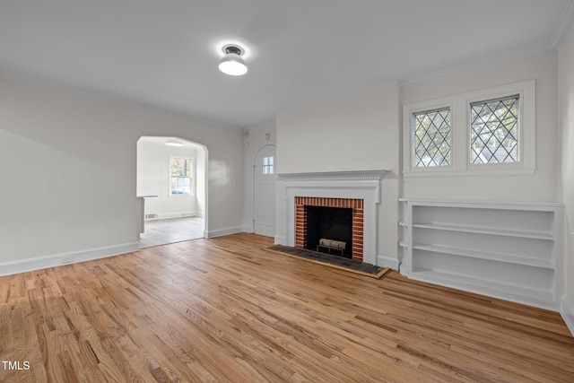 unfurnished living room with a brick fireplace, light hardwood / wood-style flooring, ornamental molding, and a healthy amount of sunlight