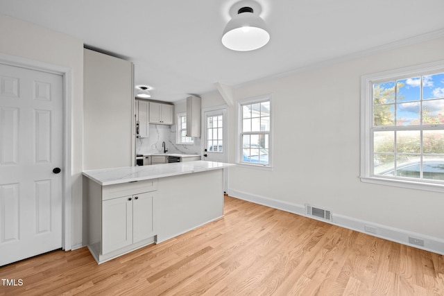 kitchen featuring white cabinets, light hardwood / wood-style floors, a healthy amount of sunlight, and kitchen peninsula