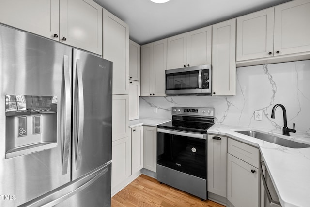 kitchen featuring stainless steel appliances, sink, tasteful backsplash, light stone countertops, and light wood-type flooring