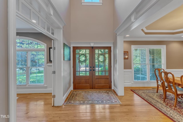 foyer entrance featuring wood finished floors, a decorative wall, a wainscoted wall, french doors, and crown molding