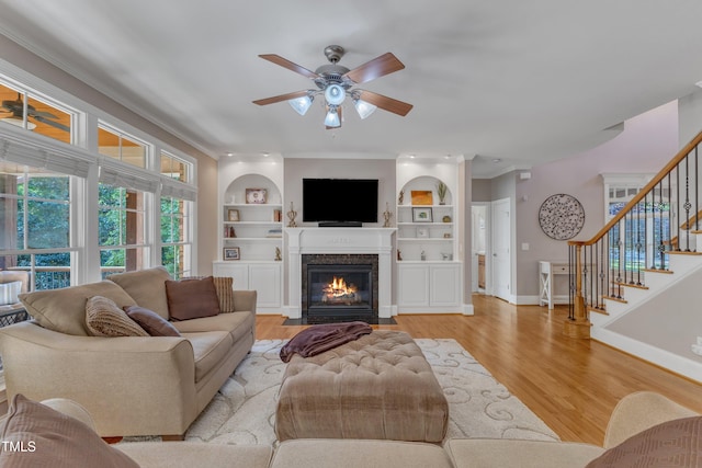 living area with a fireplace with flush hearth, crown molding, stairway, ceiling fan, and light wood-type flooring