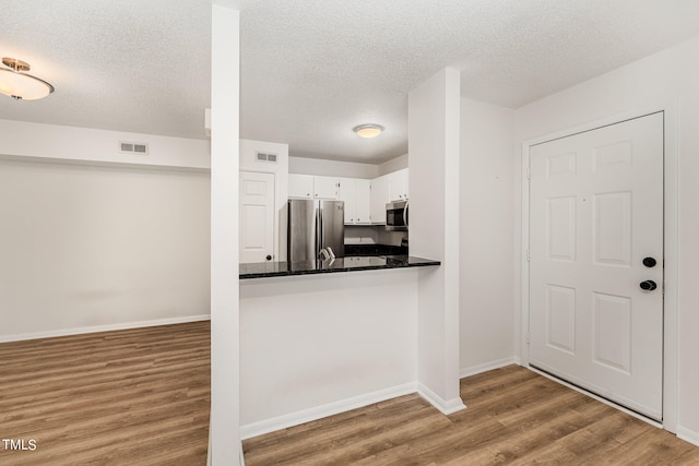 kitchen with dark stone counters, stainless steel appliances, white cabinetry, and light hardwood / wood-style flooring