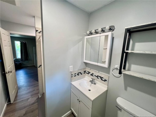 bathroom with wood-type flooring, tasteful backsplash, vanity, and toilet