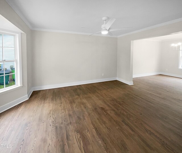 spare room featuring ceiling fan with notable chandelier, a wealth of natural light, dark wood-type flooring, and crown molding