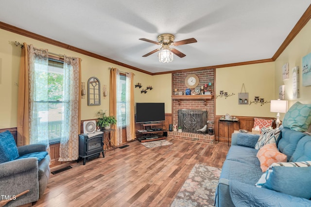 living room with a brick fireplace, a wood stove, ornamental molding, hardwood / wood-style flooring, and ceiling fan