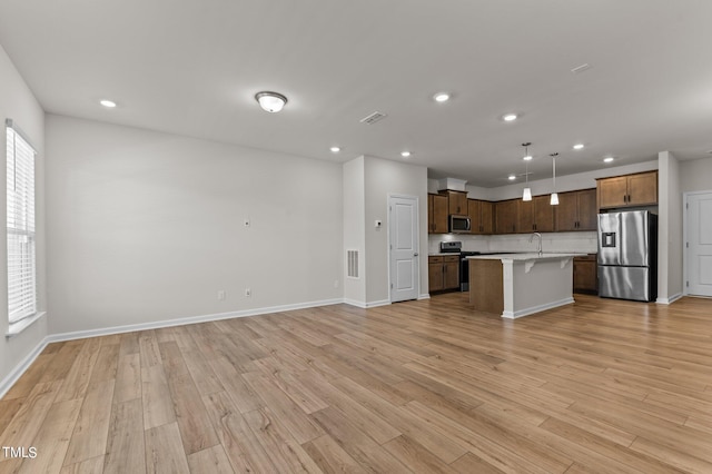 kitchen with stainless steel appliances, light wood-type flooring, a center island with sink, and hanging light fixtures