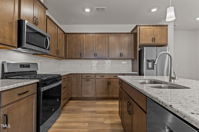 kitchen featuring sink, light stone countertops, pendant lighting, light wood-type flooring, and appliances with stainless steel finishes