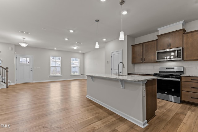 kitchen with light stone counters, stainless steel appliances, light wood-type flooring, and an island with sink