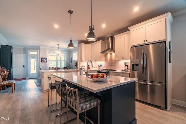 kitchen with pendant lighting, white cabinets, a center island with sink, wall chimney exhaust hood, and stainless steel appliances