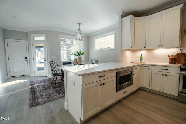 kitchen with stainless steel appliances, a peninsula, white cabinetry, hanging light fixtures, and light countertops