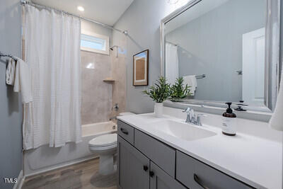 bathroom featuring toilet, wood finished floors, shower / bath combination with curtain, and vanity