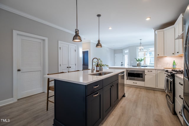 kitchen with a center island with sink, hanging light fixtures, stainless steel appliances, light countertops, and white cabinetry