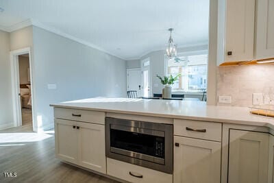 kitchen featuring hanging light fixtures, white cabinetry, stainless steel microwave, and light countertops