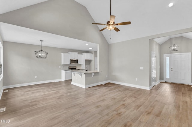 unfurnished living room featuring ceiling fan with notable chandelier, light hardwood / wood-style flooring, sink, and high vaulted ceiling