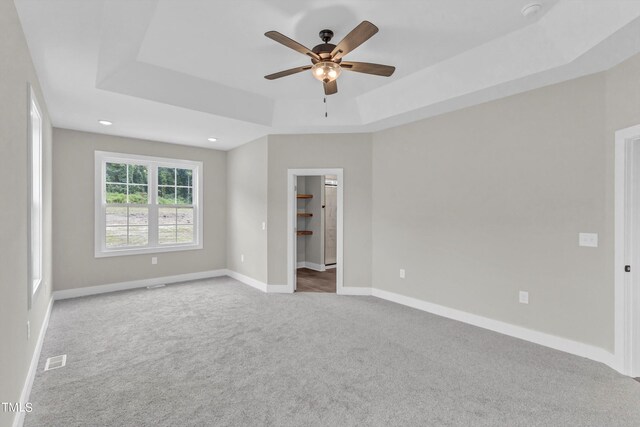 unfurnished bedroom featuring a raised ceiling, a closet, ceiling fan, a walk in closet, and carpet