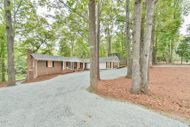 ranch-style house with gravel driveway, brick siding, a chimney, and an outbuilding