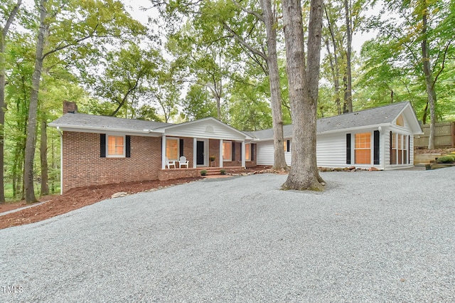 ranch-style house with gravel driveway, brick siding, a chimney, and covered porch