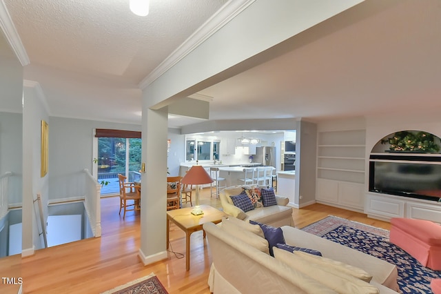 living area featuring a textured ceiling, light wood-style flooring, baseboards, built in features, and ornamental molding