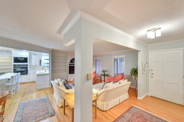 foyer entrance featuring light wood-style floors, ornamental molding, a textured ceiling, and baseboards