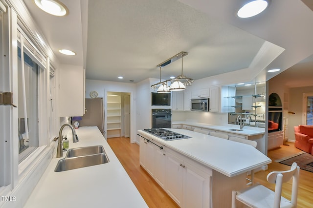 kitchen featuring a sink, white cabinetry, light countertops, appliances with stainless steel finishes, and decorative light fixtures