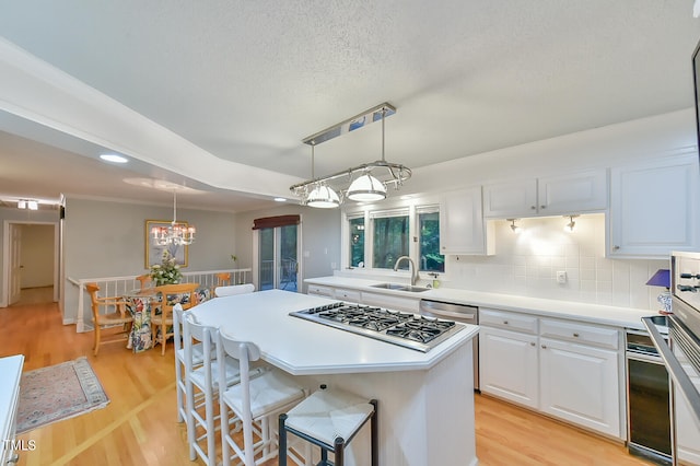 kitchen featuring a center island, decorative light fixtures, light countertops, white cabinetry, and a sink