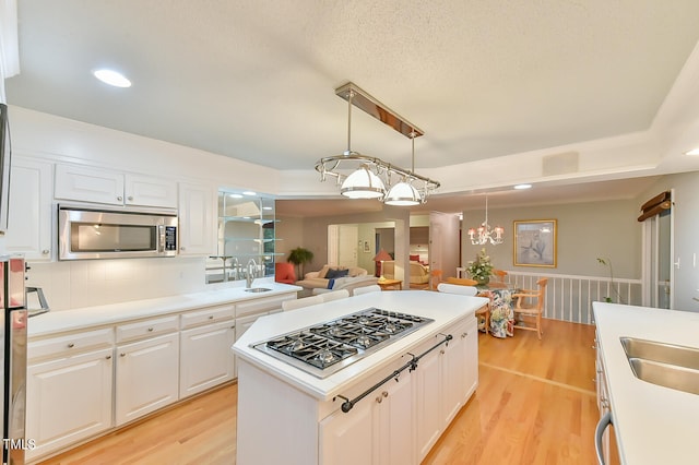 kitchen featuring light wood-style flooring, stainless steel appliances, white cabinets, hanging light fixtures, and light countertops