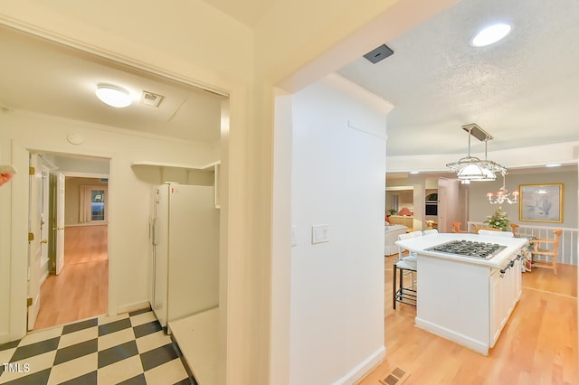 hallway featuring light floors, baseboards, visible vents, and a textured ceiling