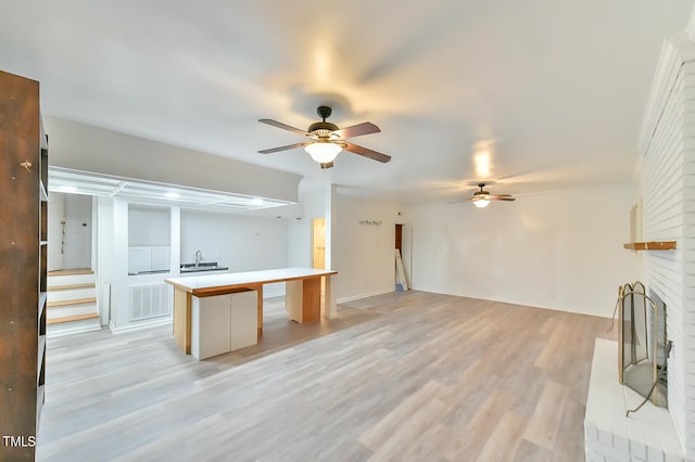 unfurnished living room with ceiling fan, a fireplace, stairs, and light wood-style flooring