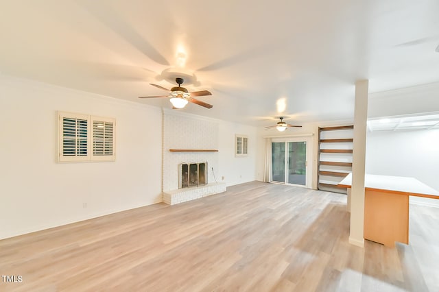 unfurnished living room featuring a brick fireplace, ceiling fan, light wood finished floors, and crown molding