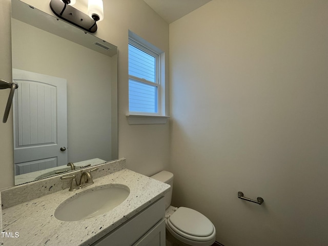 half bath featuring visible vents, vanity, and toilet