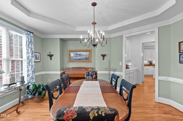 dining space with ornamental molding, light wood-type flooring, a tray ceiling, and a healthy amount of sunlight