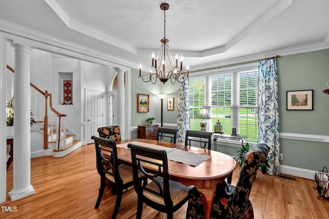 dining area with light hardwood / wood-style flooring, decorative columns, and a raised ceiling