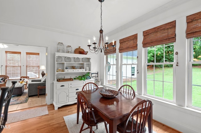 dining space with light wood-type flooring, ornamental molding, and a notable chandelier