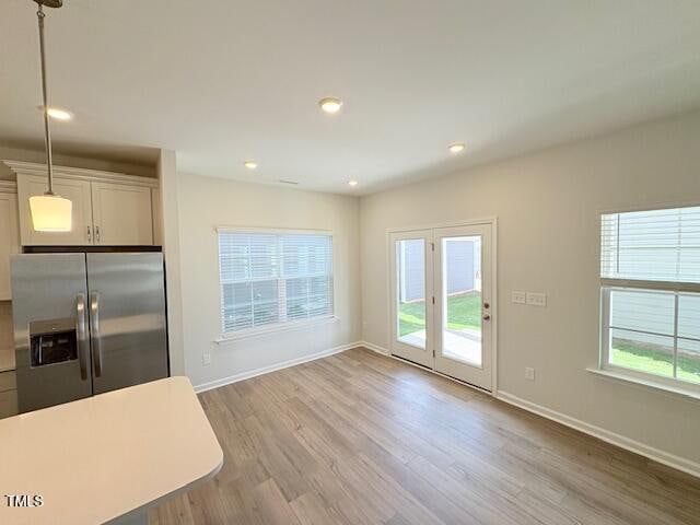 kitchen featuring stainless steel refrigerator with ice dispenser, white cabinets, light wood-type flooring, and pendant lighting