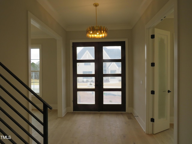 foyer entrance with french doors, ornamental molding, light hardwood / wood-style floors, and a notable chandelier