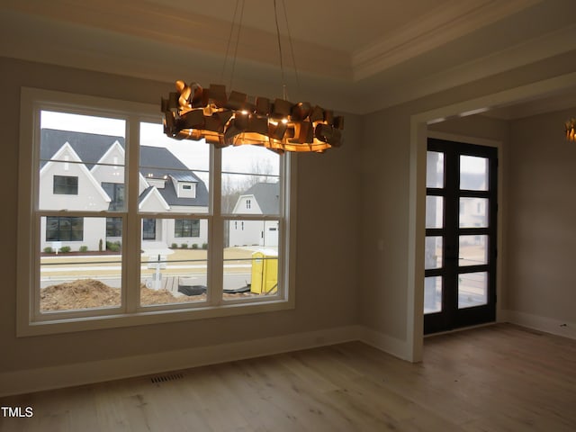 unfurnished dining area featuring ornamental molding, a tray ceiling, hardwood / wood-style floors, and a notable chandelier