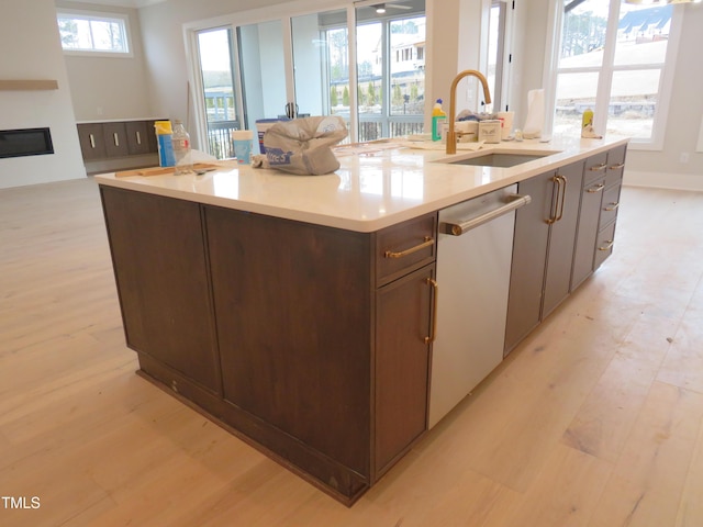 kitchen featuring an island with sink, sink, stainless steel dishwasher, and light hardwood / wood-style floors