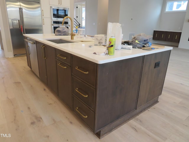 kitchen with built in appliances, sink, a kitchen island with sink, and light wood-type flooring