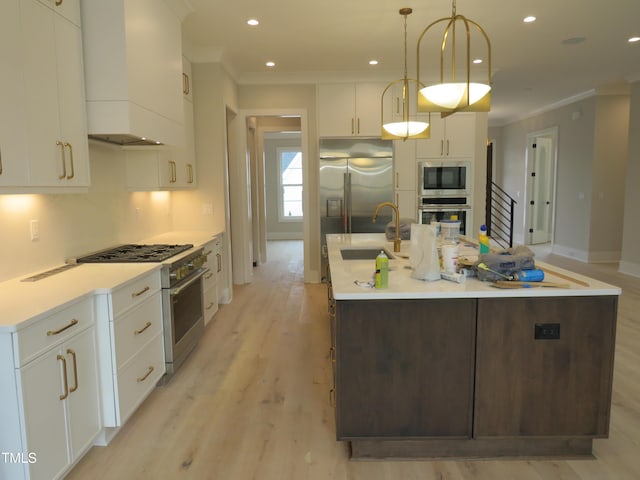 kitchen featuring decorative light fixtures, white cabinetry, built in appliances, custom range hood, and a center island with sink