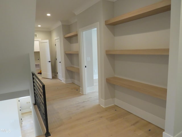 hall with built in shelves, crown molding, and light wood-type flooring