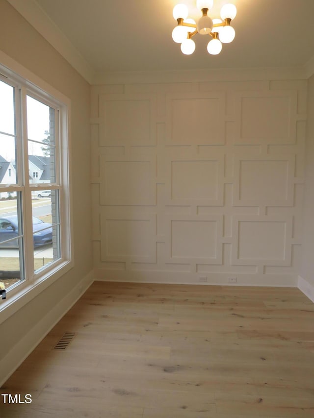 spare room with an inviting chandelier, crown molding, and light hardwood / wood-style flooring