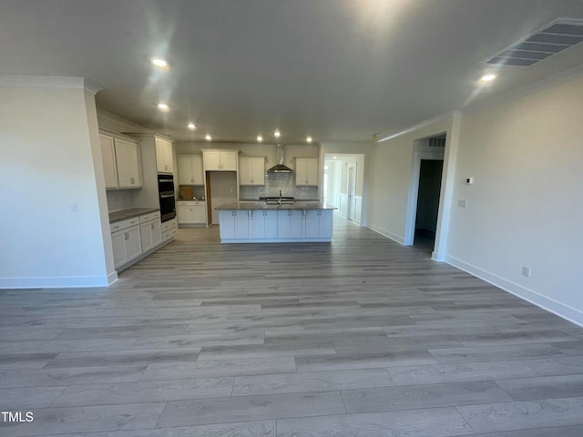 kitchen featuring a kitchen island with sink, sink, wall chimney exhaust hood, light hardwood / wood-style floors, and white cabinetry