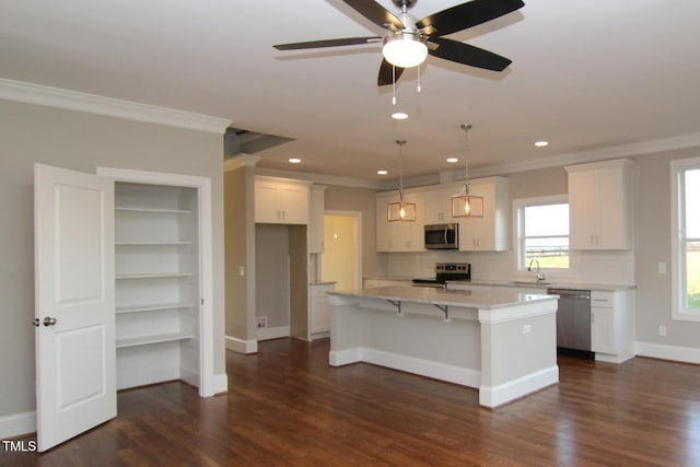 kitchen featuring white cabinetry, hanging light fixtures, appliances with stainless steel finishes, a kitchen island, and ornamental molding