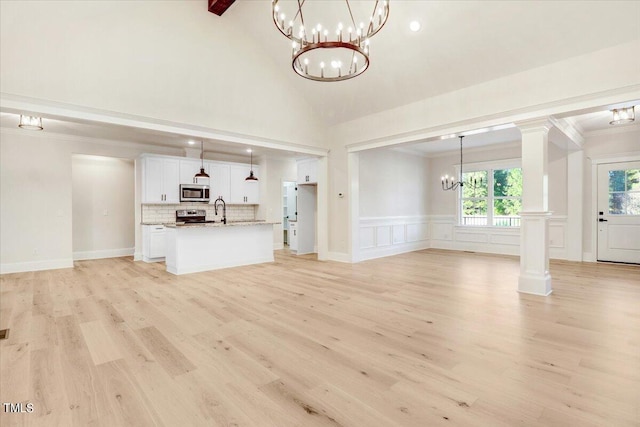 unfurnished living room with light wood-type flooring, crown molding, sink, and a notable chandelier