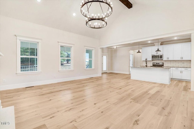 unfurnished living room featuring high vaulted ceiling, beamed ceiling, light hardwood / wood-style flooring, sink, and a chandelier