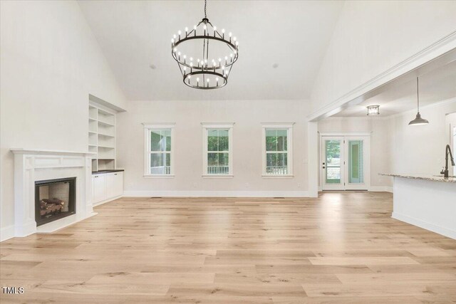 unfurnished living room featuring a high end fireplace, high vaulted ceiling, light hardwood / wood-style flooring, and plenty of natural light