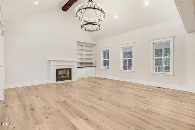 unfurnished living room featuring high vaulted ceiling, beamed ceiling, light hardwood / wood-style flooring, a chandelier, and a premium fireplace